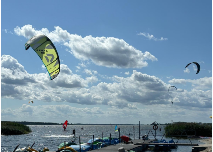**Alt-Text:** Kitesurfer auf dem Kamieński Haff bei Dziwnówek mit Tretbooten und blauem Himmel.