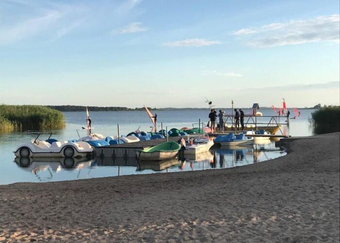 Tretboote und kleine Boote an einem Strand am Wasser.