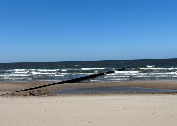 Ruhiger Sandstrand mit Blick auf die Ostsee unter blauem Himmel.