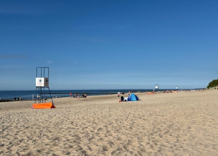 Breiter Sandstrand mit Blick auf die Ostsee und einen Rettungsturm.