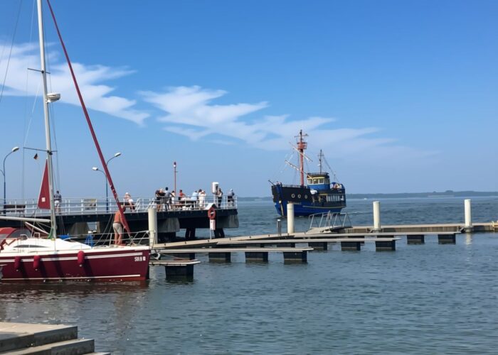 **Alt-Text:** Hafen in Dziwnów mit Ausflugsschiff, Segelbooten und Anleger an der Ostsee.
