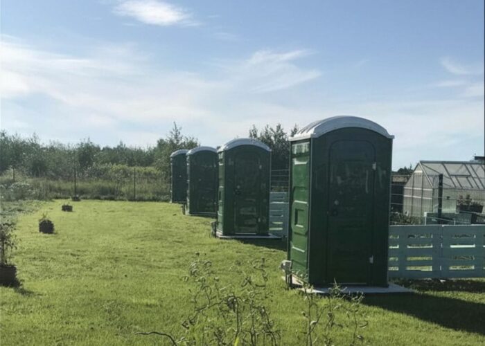 Grüne WC-Kabinen auf einer Wiese am Campingplatz.