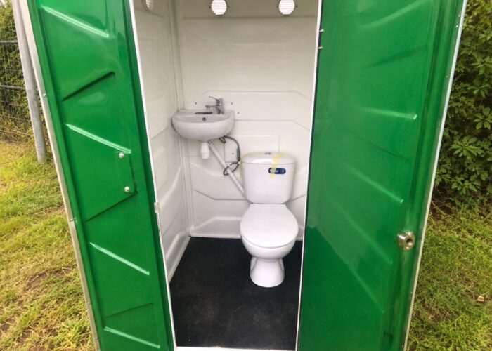 Innenansicht einer grünen WC-Kabine mit Waschbecken und Toilette.