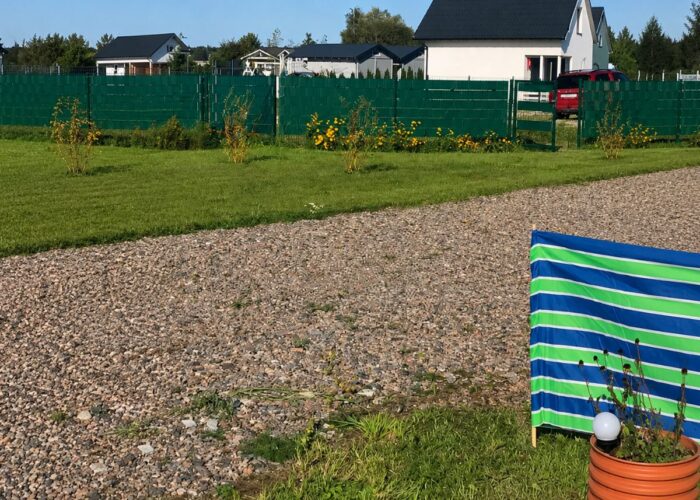 Stellplatz mit Schotterfläche, Rasen und grüner Einzäunung auf dem Campingplatz.